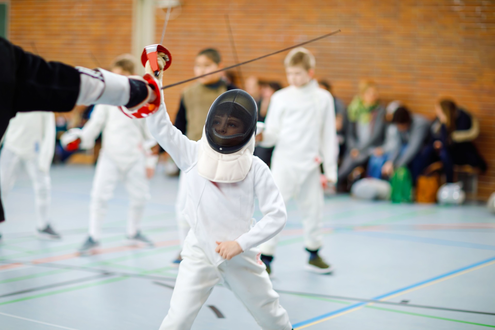 Kid niño cercado en un concurso de cerca. Niño en uniforme con sable y la máscara de blanco tirador. Chico activo entrenamiento con maestros y niños. Ocio y deportes sanos.